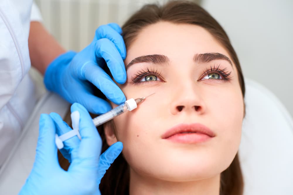 Doctor in medical gloves injects fillers in under eyes.